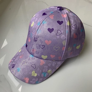 Detail of purple baseball cap featuring colorful heart patterns and glittery texture