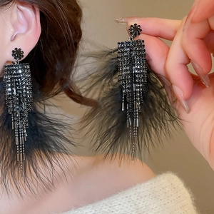 Gros plan de boucles d'oreilles noires à plumes et pompons en cristal sur un modèle