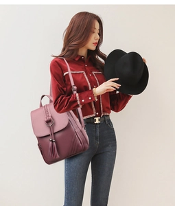 Dettaglio di zaino in pelle bordeaux con frange e manico intrecciato indossato da modella