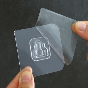 Transparent adhesive wall hook patch for router mounting being peeled by hand