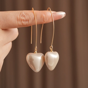 Detailed close-up of golden heart-shaped pearl earrings held between fingers