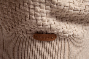 Macro shot of beige knit fabric texture with leather brand patch and metal rivets