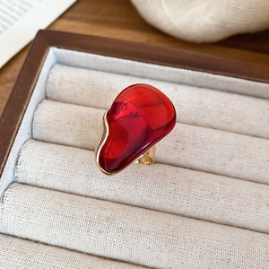 Détail d'une bague dorée avec pierre ovale en résine rouge foncé sur fond de style vintage
