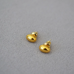 Detailed close-up of gold polished oval bean studs on textured gray background