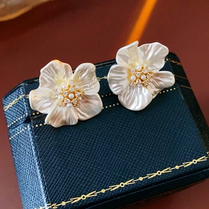 Close-up of gold-plated flower stud earrings with white petals and zircon center