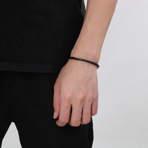 Close-up of a minimalist black woven bracelet worn on a wrist against a plain background