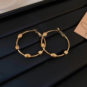 Detail of gold geometric hoop earrings with metal beads on dark leather background