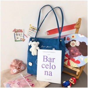 Detailed shot of blue corduroy tote bag with bear charm and embroidered text on desk