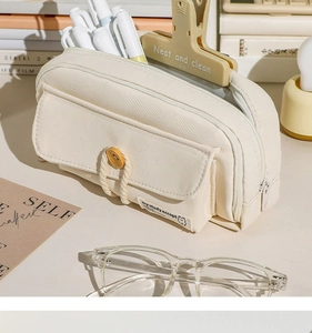 Close-up of a cream canvas pencil case with button closure and dual zippers on desk