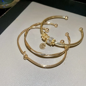 Détail d'un ensemble de trois bracelets dorés avec nœud torsadé et breloques zircon