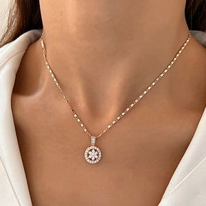Close-up of golden necklace featuring a round pendant with a diamond flower pattern