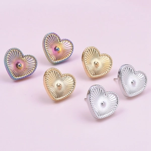 Macro detail of heart-shaped earrings in rainbow, gold, and silver on pink background