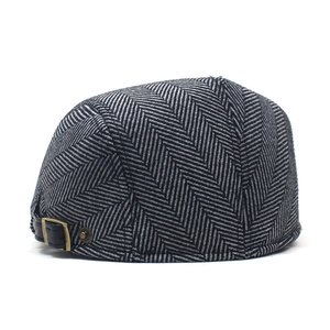 Detail of grey herringbone beret cap showing leather strap and brass adjustment buckle