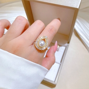 Detail view of a gold-tone pearl ring with halo of rectangular stones on index finger