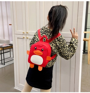 Rear view of a girl wearing a red penguin backpack with orange flippers and white belly
