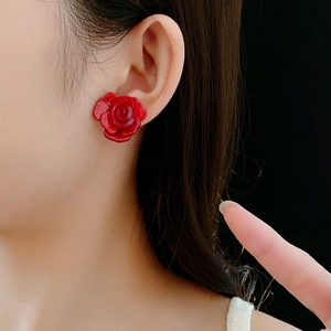 Gros plan d'une boucle d'oreille rose rouge en résine portée sur fond noir mat