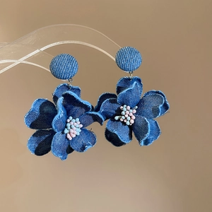 Close-up of denim fabric flower earrings with pink pearl beads and fringe edges