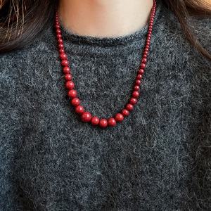Gros plan d'un collier de perles rouges élégant avec dégradé sur un pull gris chic