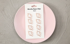 Detail view of 8 gold planet shaped paper clips on a white card inside a pink tray