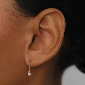 Detailed close-up of gold tassel pearl earrings with zircon inlay on a model's ear