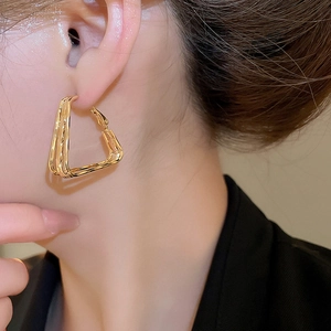 Close-up of 18k gold-plated geometric triangle hoop earrings worn by a model