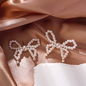 Detail of bow-shaped pearl earrings with gold base on elegant champagne satin fabric