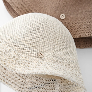 Détail d'un chapeau bob en maille avec tissage ajouré et logo métallique doré JS gravé