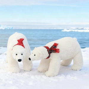 Plush white polar bear dolls with festive scarves standing on snow by the sea