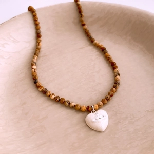 Close-up of beaded brown stone necklace with white heart orb pendant on a ceramic dish