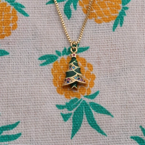 Close-up of gold-plated Christmas tree pendant with green enamel and colorful rhinestones