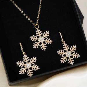 Golden snowflake jewelry set with zirconia stones in black gift box on beige silk background