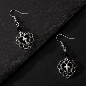 Macro shot of silver heart-shaped drop earrings with a central cross and black bead detail