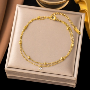Double-layered gold beaded anklet with crystal pendant on a beige silk jewelry box