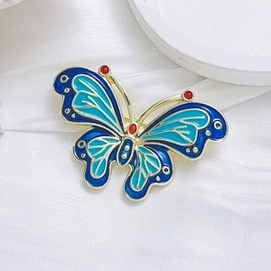 Elegante broche de mariposa en esmalte azul y verde con baño de oro y gemas rojas