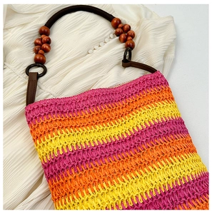 Detail view of woven straw tote bag featuring rainbow gradient and wooden bead handle