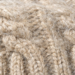 Close-up of thick beige cable knit texture and soft fuzzy mohair yarn details for winter hat