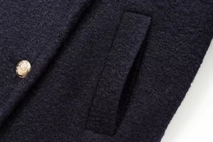 Macro detail of dark textured wool coat fabric with a vintage golden lion emblem button
