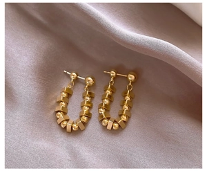 Close-up of gold U-shaped earrings with geometric beads on soft silk fabric