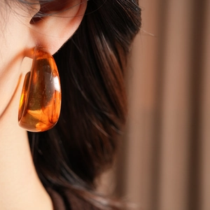 Close-up of amber resin C-shaped hoop earring worn by a model in a retro style