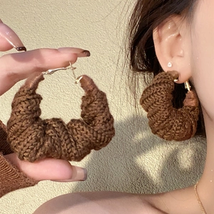 Close-up of brown knitted twist hoop earrings worn by a model in soft lighting