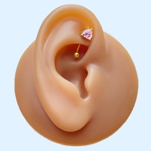 Detailed macro view of a gold curved barbell rook piercing with a pink heart zircon gem