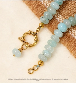 Macro shot of aquamarine crystal beads featuring a large golden spring clasp and natural texture