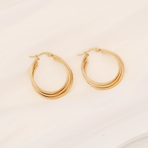 Detailed view of gold-plated triple hoop earrings on white textured fabric backdrop