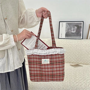 Detail view of red plaid tote bag with white lace trim and thick shoulder straps