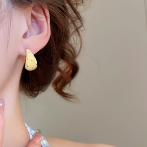 Close-up of model wearing yellow C-shaped earrings with blue polka dot pattern