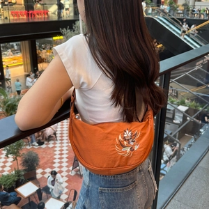 Detailed view of an orange crescent bag with floral embroidery worn on the shoulder
