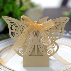 Macro shot of laser-cut gold butterfly favor box with ribbon on a white plate