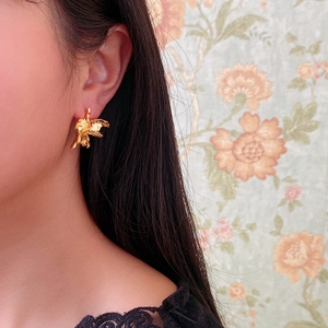 Primo piano di orecchini a fiore dorati irregolari indossati da una modella elegante