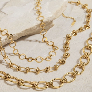 Trois styles de colliers en acier inoxydable plaqués or 18 carats sur fond de pierre