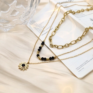 Close-up of triple-layered golden sun pendant necklace with black beads on silk background